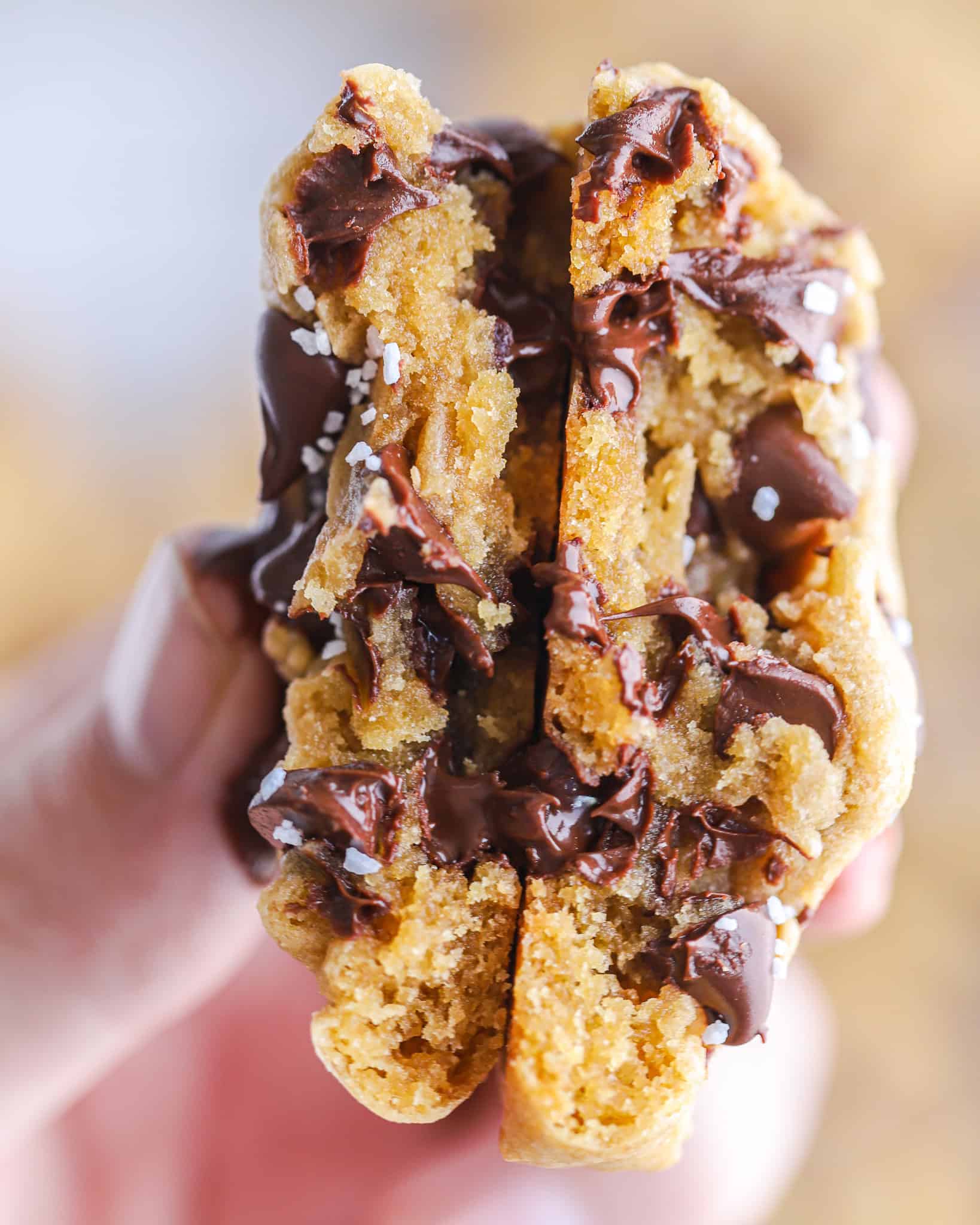 hand holding a Chocolate Chunk Cookie split in half showing the melted chocolate inside